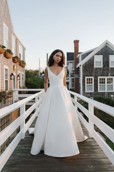 a woman in a white wedding dress is standing on a wooden bridge near some houses