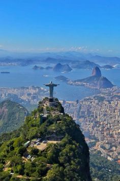 a statue on top of a mountain overlooking the city and water with mountains in the background