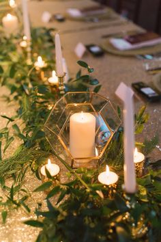 candles and greenery are lined up on the table