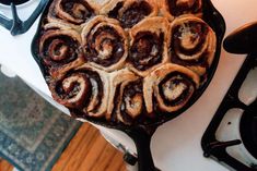 a pan filled with cinnamon rolls sitting on top of a stove next to an oven