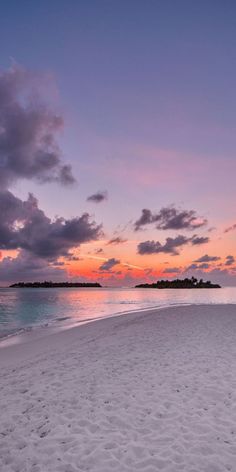 the sun is setting on an empty beach with footprints in the white sand and blue water