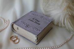 two wedding rings sitting on top of a book next to a pearl necklace and ring box