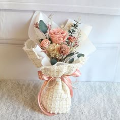 a bouquet of flowers sitting on top of a table next to a white bag with pink ribbon