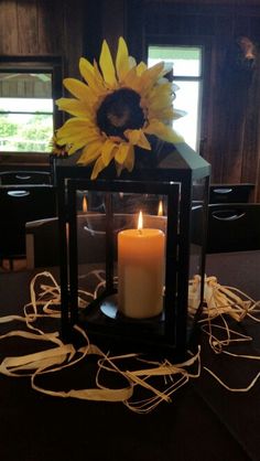 a sunflower sits on top of a table next to a lit candle