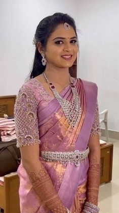 a woman in a pink and gold sari with jewelry on her neck, smiling at the camera