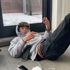 a young man sitting on the ground with his feet up in front of an open window