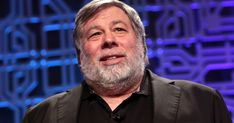 an older man with a beard and black shirt is standing in front of a blue background