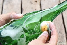 a person is holding a green bottle with soap on it and some water droplets all over it