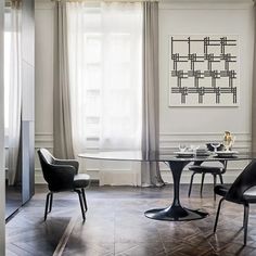 an elegant dining room with black and white chairs, a glass table and artwork on the wall