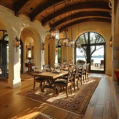 a dining room with an arched ceiling and wooden table surrounded by chairs, rugs and chandeliers