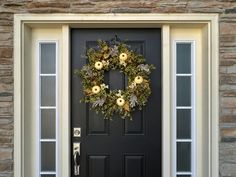 a black front door with a wreath and two pumpkins hanging on it's side