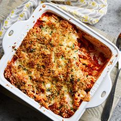 a casserole dish with meat and cheese in it on a wooden table next to a fork