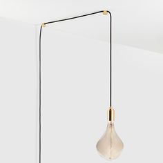 a light bulb hanging from a black cord with a white wall in the back ground