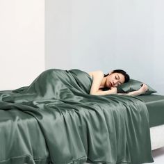 a woman laying on top of a bed covered in a green blanket