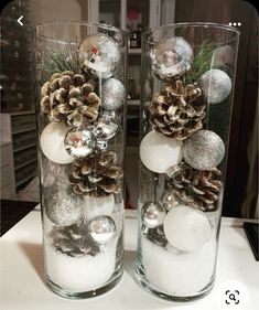 two clear vases with pine cones and balls in them sitting on a counter top