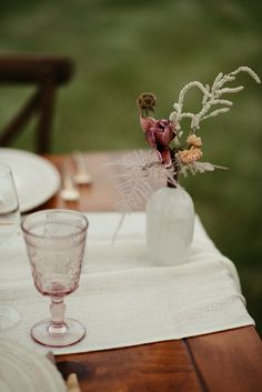 the table is set with an empty glass vase and some flowers on top of it