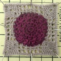 a crocheted square with pins sticking out of it and the center is purple