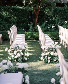 rows of chairs with white flowers and greenery in the middle of an outdoor ceremony