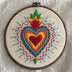 a colorful heart is embroidered on a white background with brown wood frame and metal hooks