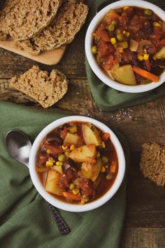 two bowls filled with stew next to slices of bread