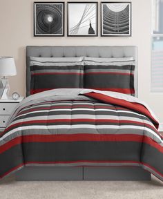 a bed with red and grey striped comforter set in a white room next to two pictures on the wall