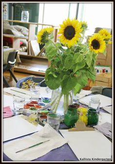 sunflowers in a vase sitting on top of a table covered with papers and paint