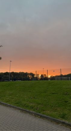 the sun is setting over a grassy field in front of a fenced in area