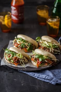 four sandwiches with meat, lettuce and sauce on a plate next to drinks