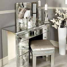 a mirrored vanity with a stool and flowers in a vase on the table next to it