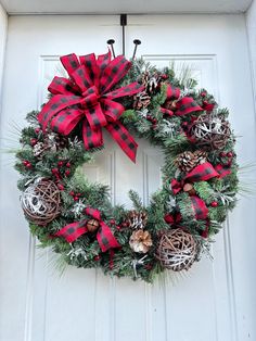 a christmas wreath hanging on the front door with pine cones and red plaid bow tie