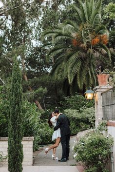 a bride and groom kissing in front of a palm tree at the end of their wedding day