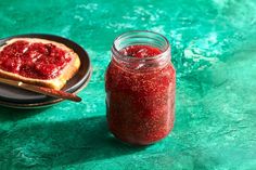 a glass jar filled with jam next to a slice of bread on a black plate