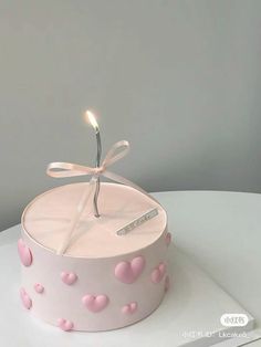 a pink cake with hearts on it and a single lit candle in the middle that says love