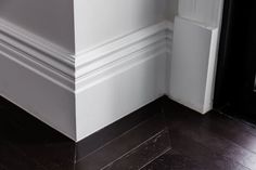 the corner of a room with white walls and dark wood flooring is shown in this image