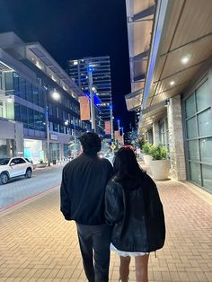 a man and woman walking down the street at night with their backs to each other