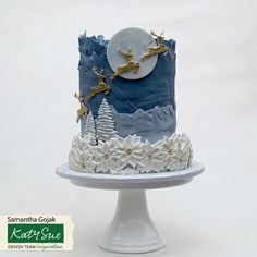 a blue and white christmas cake with reindeers on the top is sitting on a pedestal