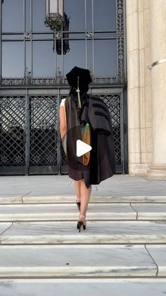 a woman walking down the street in front of a building wearing a black robe and hat