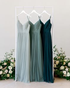 three bridesmaid dresses hanging on a rack in front of flowers