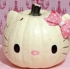 a hello kitty pumpkin with a pink bow on it's head is sitting in front of a wall