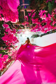 a woman in a long pink dress is standing under flowers