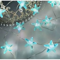 blue star lights are hanging from a wire on a table next to pearls and a tiara