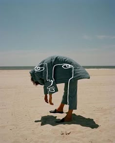 a person bending over in the sand with their head under a blanket on top of them