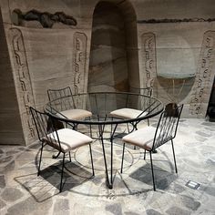 a glass table with four chairs in front of an artisticly designed stone wall and floor