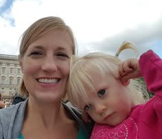 a woman holding a child in front of a building with people standing around and looking at the camera