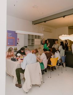 a group of people sitting at tables eating food in a room with white walls and flooring