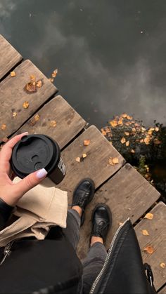 a person sitting on a dock holding a coffee cup with their thumb up to the camera