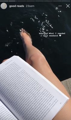 someone is reading a book while sitting on the edge of a dock with their feet in the water