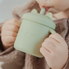 a baby drinking from a green cup with a cat face on it's side