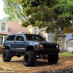 a blue jeep parked in front of a house on a leaf covered driveway next to a tree