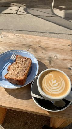 a cup of coffee next to a piece of bread on a plate with a spoon